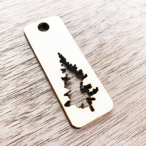 May include: A wooden tag with a cutout of a pine tree. The tag has a hole at the top for hanging.