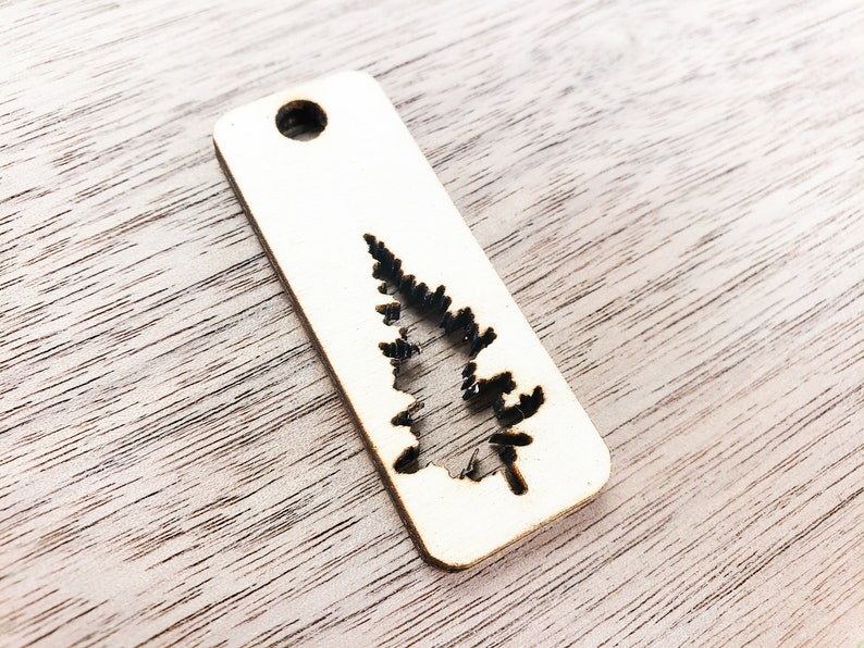 May include: A wooden tag with a cutout of a pine tree. The tag has a hole at the top for hanging.