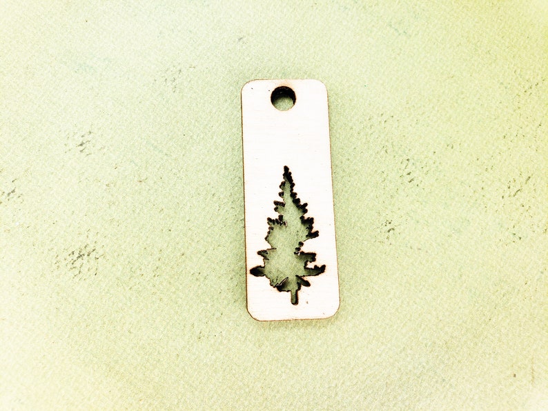 May include: A wooden tag with a cutout of a pine tree. The tag has a hole at the top for hanging.