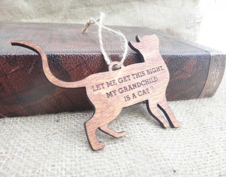 May include: Wooden cat ornament with the text "Let me get this right. My grandchild is a cat?"