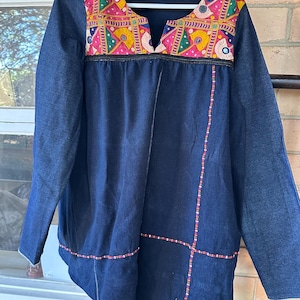 May include: A dark blue denim tunic with colourful embroidery and beaded trim. The embroidery features geometric patterns and small mirrors.