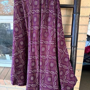 May include: A long, flowing skirt in a deep purple hue, adorned with a repeating pattern of white and tan floral designs. The skirt is made of a lightweight fabric and appears to have a drawstring or elastic waistband.