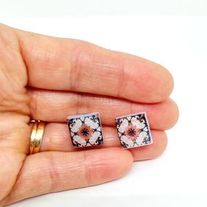 K&ouml;nnte beinhalten: Ein Paar quadratische Ohrringe mit einem rosa-wei&szlig;en Blumendesign auf wei&szlig;em Hintergrund. Die Ohrringe sind aus Harz gefertigt und haben eine gl&auml;nzende Oberfl&auml;che.