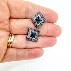 K&ouml;nnte beinhalten: Zwei quadratische Glasfliesen mit einem blauen und wei&szlig;en Blumenmuster. Die Fliesen sind vor einem wei&szlig;en Hintergrund platziert.
