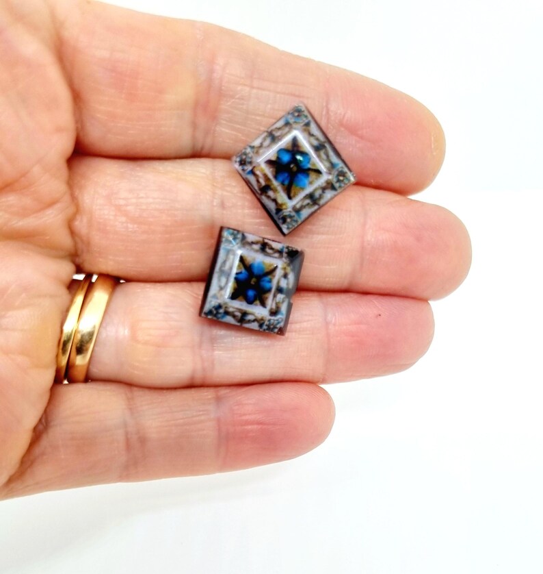 K&ouml;nnte beinhalten: Zwei quadratische Glasfliesen mit einem blauen und wei&szlig;en Blumenmuster. Die Fliesen sind vor einem wei&szlig;en Hintergrund platziert.