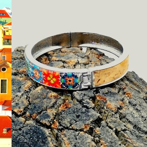 Peut inclure: Un bracelet jonc argenté avec un incrustation en liège et un motif coloré. Le bracelet est posé sur une surface rugueuse, brune et texturée.