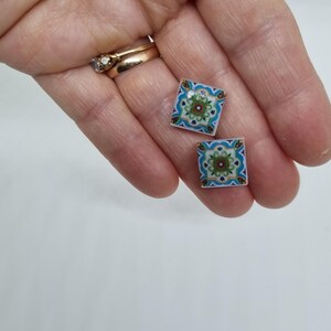 K&ouml;nnte beinhalten: Ein Paar quadratische Ohrringe mit einem bunten geometrischen Muster. Die Ohrringe sind blau, gr&uuml;n, wei&szlig; und gold.