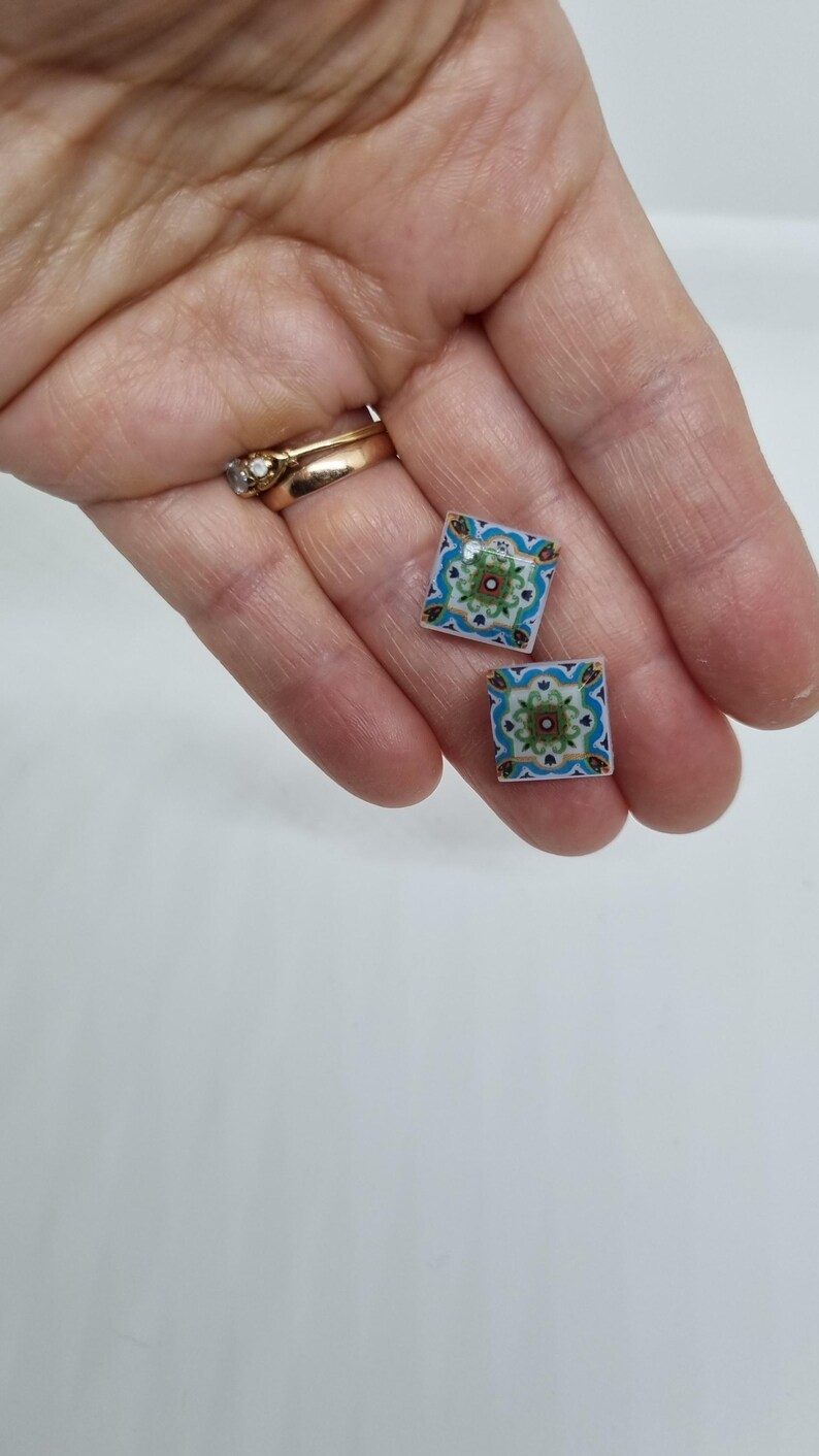 K&ouml;nnte beinhalten: Ein Paar quadratische Ohrringe mit einem bunten geometrischen Muster. Die Ohrringe sind blau, gr&uuml;n, wei&szlig; und gold.
