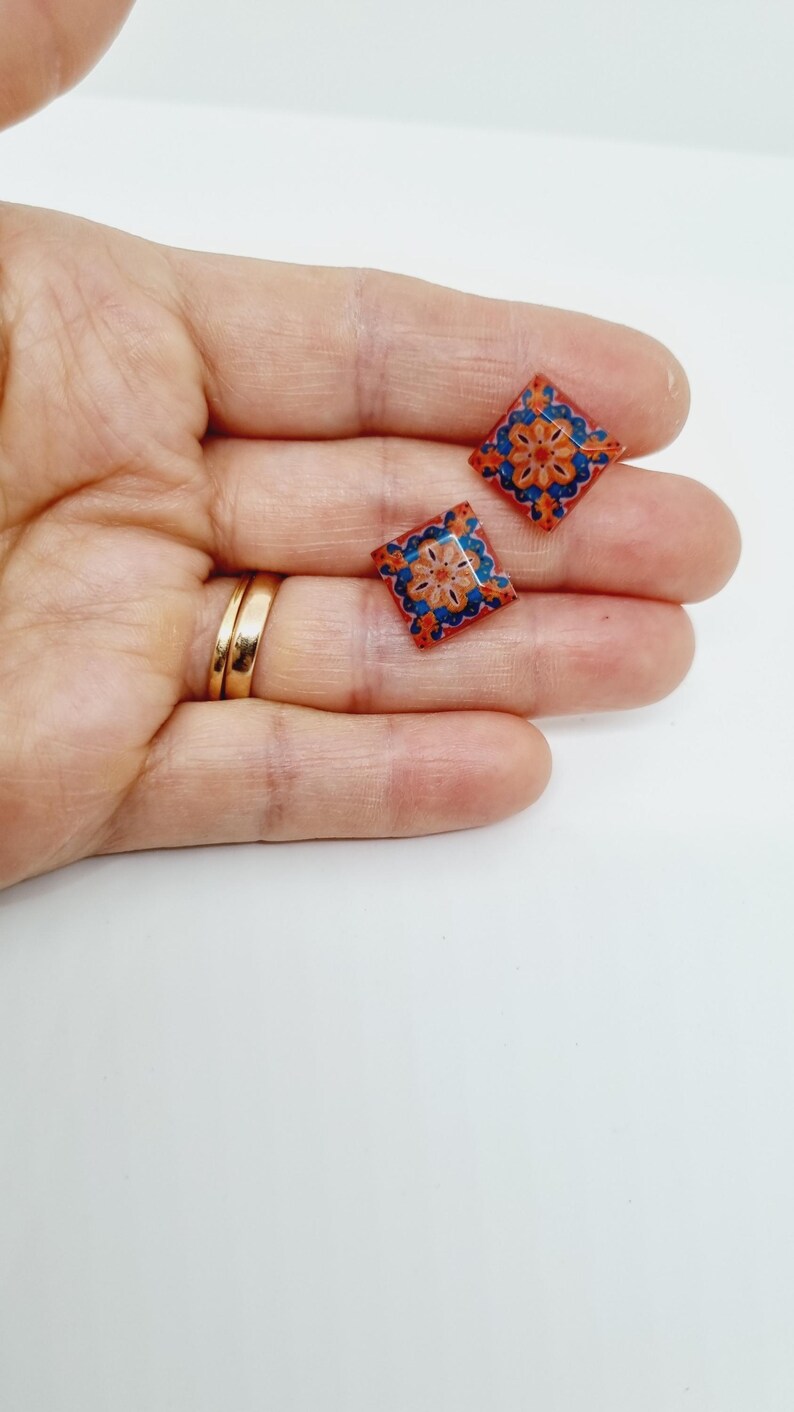 K&ouml;nnte beinhalten: Ein Paar kleine, quadratische Ohrringe mit einem bunten geometrischen Muster. Die Ohrringe sind rot, orange, blau und wei&szlig;.