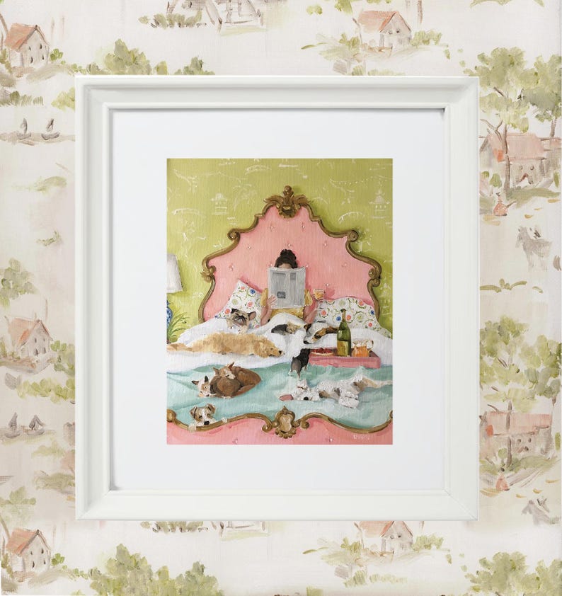 May include: A framed print depicts a cozy scene of a person reading in bed, surrounded by several dogs. The bed has a pink headboard and a green patterned background. A tray with food and drinks sits on the bed. The frame is white.