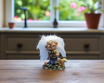 May include: A whimsical figurine of a troll with a large white fluffy hairstyle, holding flowers, and seated next to a squirrel. The troll wears blue pants. The figurine is on a base with flowers and greenery.