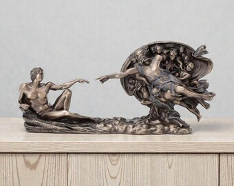 May include: A bronze-colored sculpture depicting the iconic scene of the Creation of Adam from the Sistine Chapel ceiling. The sculpture features two figures, one reclining and the other reaching out, with intricate details.