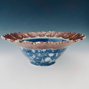 May include: A large, blue and white ceramic bowl with a brown, leafy rim. The bowl has a speckled glaze and a unique, organic shape.