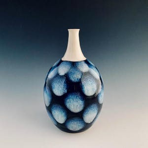 May include: A ceramic vase with a rounded body and a slender neck. The vase is dark blue with a pattern of light blue, irregular circles. The neck is a smooth, off-white colour.