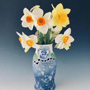 May include: A blue and white ceramic vase with a floral design and cutouts. The vase is filled with a bouquet of yellow and white daffodils.