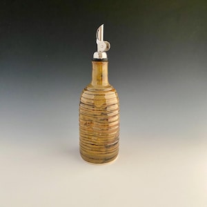 May include: A ceramic olive oil bottle with a stainless steel spout. The bottle has a textured, horizontal striped design in shades of brown and tan. The spout is silver and has a hinged cap.