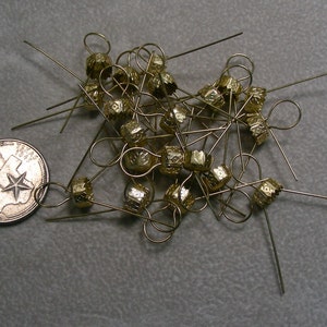 May include: A pile of gold-colored metal ornament caps with loops. The caps have a decorative design and are used for hanging ornaments on a Christmas tree.