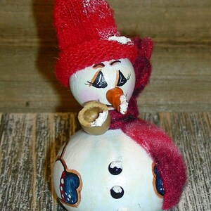 Pu&ograve; includere: Ornamento a forma di pupazzo di neve dipinto a mano con cappello e sciarpa rossi a maglia. Il pupazzo di neve ha un naso a carota, occhi neri e una tazza piccola. L'ornamento &egrave; decorato con dettagli blu e rossi e tre bottoni neri.