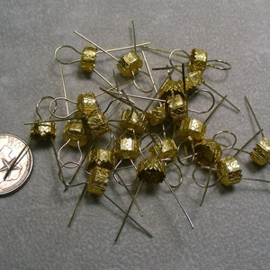 May include: A pile of gold-colored metal ornament caps with wire loops. The caps have a decorative, geometric pattern.