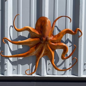 May include: Orange octopus wall decor with eight tentacles. The octopus is mounted on a white metal wall.