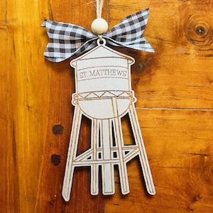 May include: Wooden ornament shaped like a water tower with the text "ST. MATTHEWS" on the side. The ornament is decorated with a black and white checkered bow.