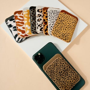 May include: A set of ten phone wallet cases with different animal print designs. The cases are made of leather and have a variety of colors, including brown, black, white, and tan. The cases are arranged in a row, with the most colorful case at the front.