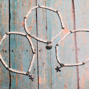 May include: Three white shell bead anklets with silver charms. The charms are a seashell, a starfish, and a turtle.