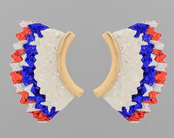 May include: A pair of gold hoop earrings with a white, red, and blue glitter design. The design resembles a fan or a firework.
