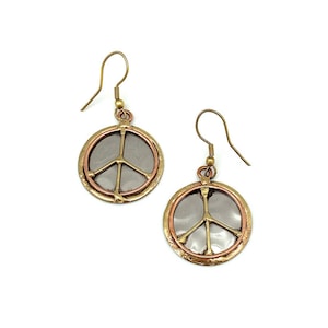May include: A pair of gold and copper peace sign earrings. The earrings are round and have a peace sign design in the center. The peace sign is made of a silver metal.