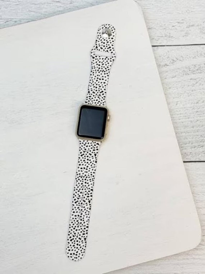 May include: A white and black polka dot Apple Watch band. The band is made of silicone and has a sleek, modern design.