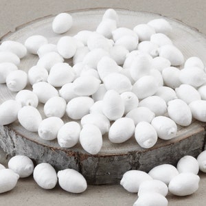 Op de afbeelding: Een stapel witte, ronde, papierachtige voorwerpen, die lijken op kleine eieren, op een houten oppervlak.