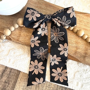 May include: A black bow with a brown floral pattern. The bow is tied with long tails.