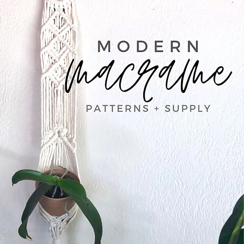 May include: A white macrame plant hanger with a small potted plant hanging inside. The text "MODERN macrame PATTERNS + SUPPLY" is written on a white wall behind the hanger.