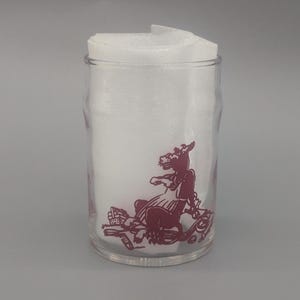 May include: A clear glass jar with a red illustration of a horse-like creature. The jar is filled with white material. The illustration is on the front of the jar.