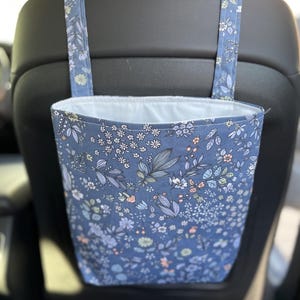 May include: A blue and white floral patterned fabric car trash bag with a white lining. The bag hangs from the headrest of a car seat.