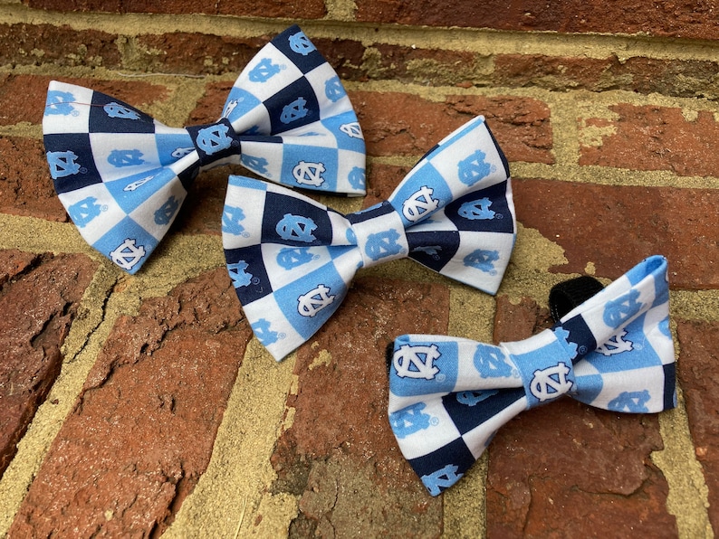 May include: Three bow ties in different sizes, all featuring a checkered pattern in blue, white, and navy blue with a repeated logo of a blue 'NC' on a white background.