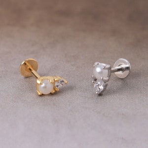 May include: Two stud earrings, one gold-toned and one silver-toned, each featuring a pearl and small clear crystals. The gold earring has a pearl and two crystals, while the silver earring has a pearl and two crystals.