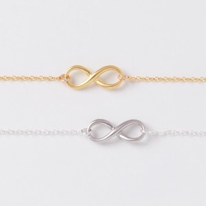 May include: Two delicate infinity symbol bracelets. One is gold-toned, the other silver-toned. Each bracelet features a chain with a small infinity charm at the center. The bracelets are displayed against a white background.