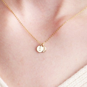 May include: A gold chain necklace with two small gold discs, each with a letter 'B' engraved on it. The necklace is 16 inches long.
