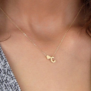 May include: A gold necklace with a small heart charm and a letter 'C' pendant. The necklace is 17 inches long.