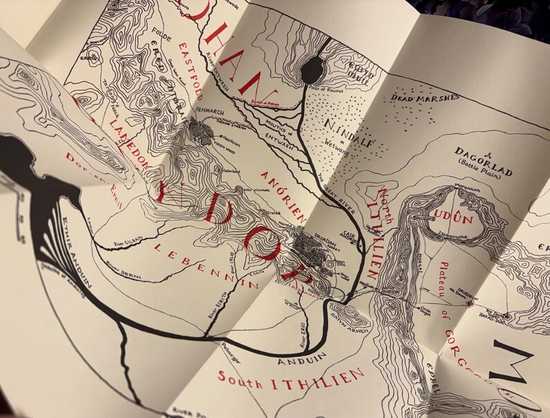 May include: A detailed map with black line art and red text, featuring geographical features and place names. The map is folded, revealing sections of a larger design. The map includes the text "Lamedon", "Udun", and "Daglorad".