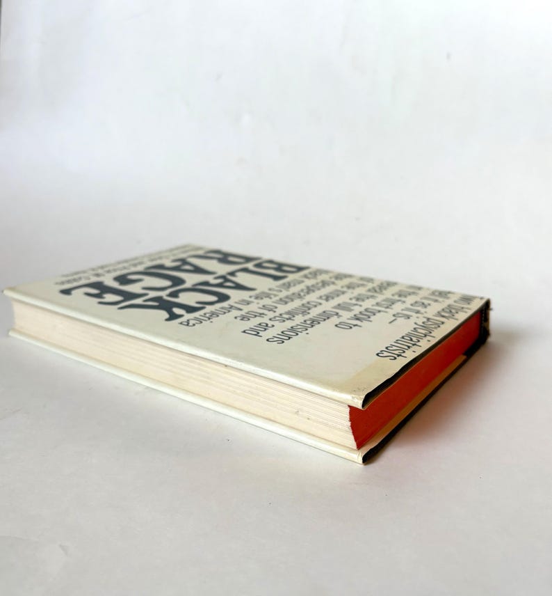 K&ouml;nnte beinhalten: Ein Buch mit dem Titel "Black Rage" mit schwarzem Text auf einem wei&szlig;en Einband. Der Buchr&uuml;cken ist schwarz und die Seiten sind cremefarben mit einem roten Rand. Das Buch ist leicht angewinkelt.