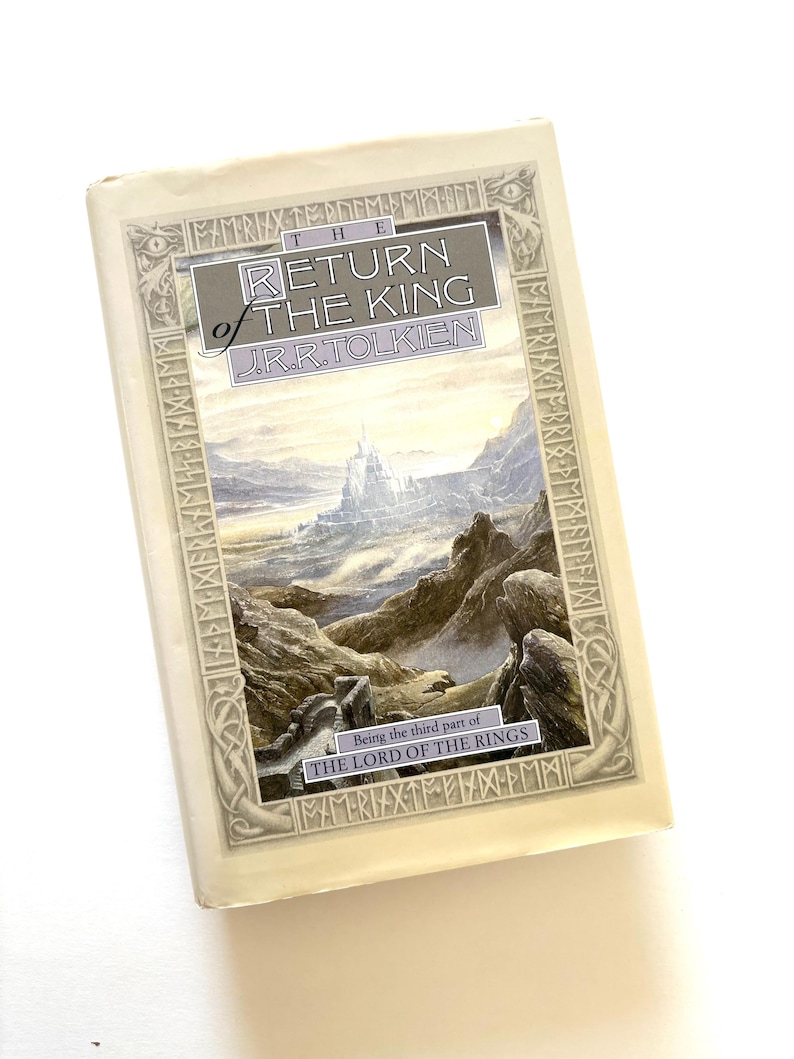 May include: A hardcover book titled "The Return of the King" by J.R.R. Tolkien, part of "The Lord of the Rings" series. The cover features a landscape illustration with a castle and mountains, framed by an ornate border. The book is in a protective cover.