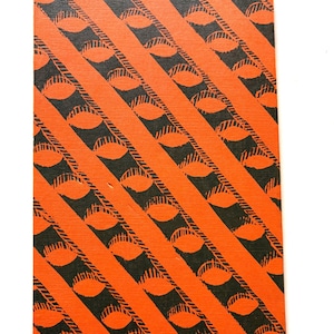 Pu&ograve; includere: Un oggetto rettangolare con un motivo ripetuto di disegni neri a forma di occhio all'interno di strisce diagonali arancioni. Il design copre l'intera superficie, creando un effetto visivo audace e grafico.