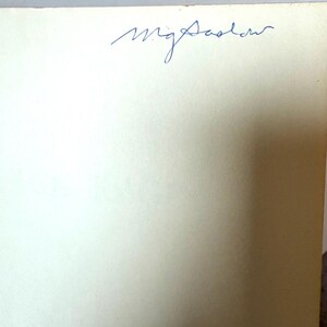 K&ouml;nnte beinhalten: Nahaufnahme eines cremefarbenen Papiers mit der handschriftlichen Signatur "mg Sadler" in blauer Tinte oben. Das Papier hat eine leicht strukturierte Oberfl&auml;che.