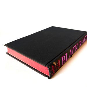 K&ouml;nnte beinhalten: Ein Hardcover-Buch mit schwarzem Einband und rosa Buchschnitt. Der Buchr&uuml;cken zeigt den Titel "BLACK RAGE" in rosa Schrift. Der Name des Autors ist ebenfalls sichtbar. Das Buch ist vor einem wei&szlig;en Hintergrund platziert.