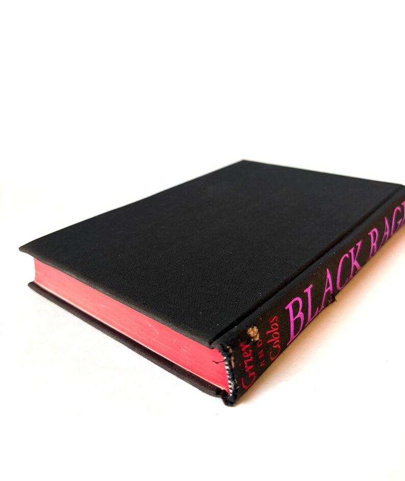 K&ouml;nnte beinhalten: Ein Hardcover-Buch mit schwarzem Einband und rosa Buchschnitt. Der Buchr&uuml;cken zeigt den Titel "BLACK RAGE" in rosa Schrift. Der Name des Autors ist ebenfalls sichtbar. Das Buch ist vor einem wei&szlig;en Hintergrund platziert.