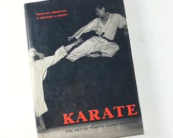 Op de afbeelding: Een zwart-witfoto van twee mensen die karate beoefenen. De omslag van het boek toont de titel "KARATE" in rode letters en de tekst "THE ART OF "EMPTY HAND" FIGHTING" in witte letters.
