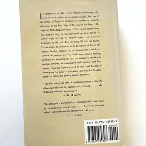 May include: A book cover for "The Lord of the Rings" by J.R.R. Tolkien. The back cover is a light beige color with black text describing the story and quotes from W.H. Auden and C.S. Lewis. The ISBN is visible.