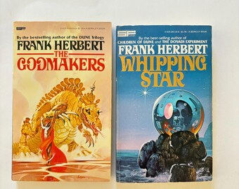 May include: Two vintage paperback books by Frank Herbert. The book on the left is titled "The Godmakers" with a gold and red illustration. The book on the right is titled "Whipping Star" with a blue and white illustration.